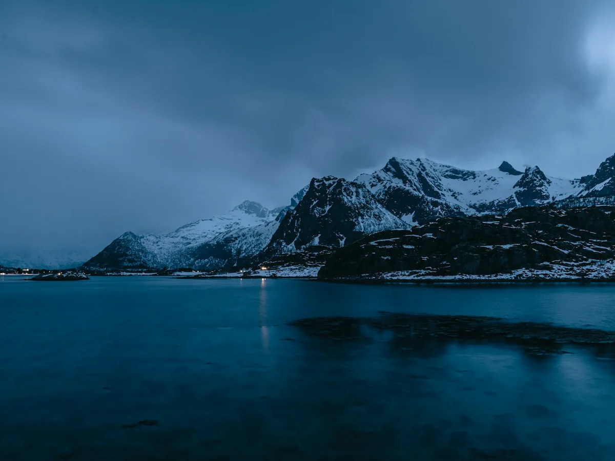 Veduta al crepuscolo di montagne artiche innevate sopra un fjord immobile, nella profonda luce blu dell'inverno